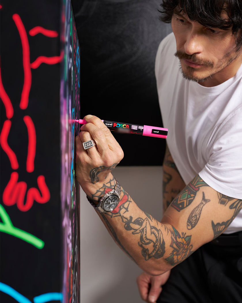 Artist using pink posca paint marker to draw neon-style artwork on black surface