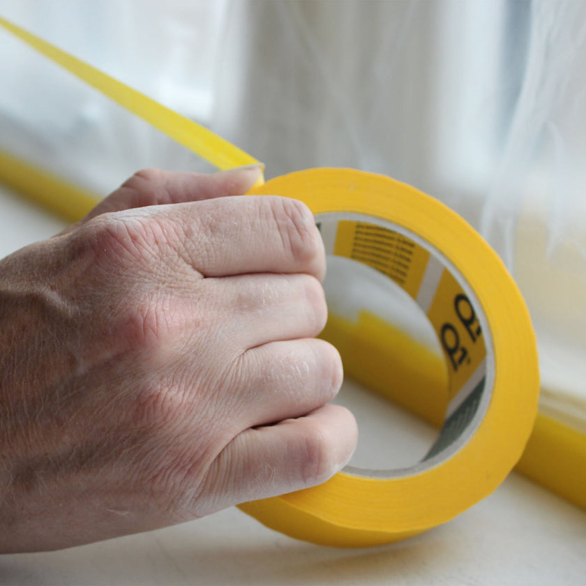 Q1 yellow masking tape roll being pulled by hand for painting and DIY use
